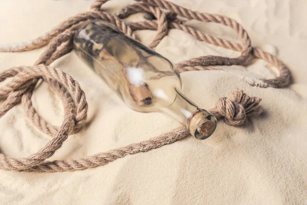 Corked bottle with message and rope on sandy beach