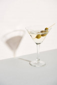 Olivy ve sklenici martini a stín na bílém pozadí