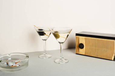 Kül tablası ve sigara izmaritli martini kokteylleri ve beyaz arka planda klasik radyo.