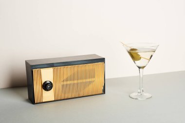 Vintage radio with glass of martini cocktail on grey surface clipart