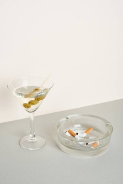 Sigara izmaritli kül tablası ve gri yüzeyde beyaz üzerine izole edilmiş bir kokteyl.