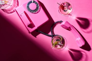 Pembe yüzey üzerinde sigara izmaritleri olan telefon ve kokteyllerin üst görüntüsü.