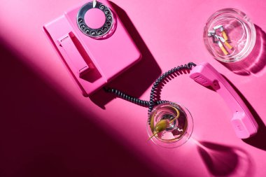 Top view of cocktail and retro telephone beside astray with cigarette butts on pink surface clipart