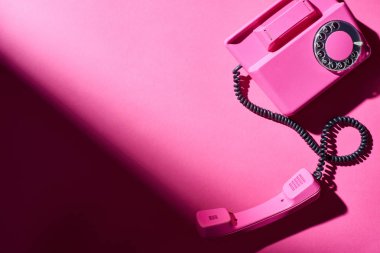 Parlak yüzeyde gölgesi olan pembe telefonun üst görüntüsü