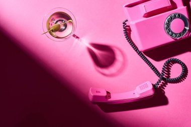 Pembe arka planda martini ve retro telefon olan cam manzaralı.