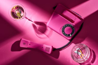 Top view of pink telephone, cocktail and astray with cigarette butts on pink surface clipart