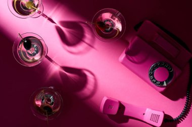 Martini kokteyllerinin ve pembe arka plandaki retro telefonun en üst görüntüsü.