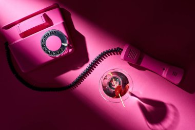 Pembe arka planda gölgesi olan klasik telefon ve kokteyllerin üst görüntüsü