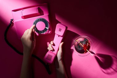 Pembe arka planda martinili retro telefon kullanan bir kadın görüntüsü.