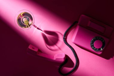 Açık pembe arka planda martini ve retro telefonun üst görüntüsü