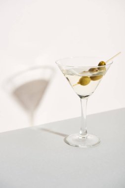 Bir bardak martinide zeytin ve beyaz arka planda gölge.