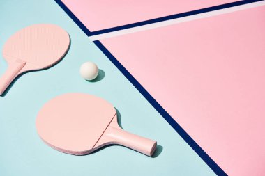 Yüksek açılı masa tenisi raketleri ve mavi çizgili pastel yüzeydeki top görüntüsü