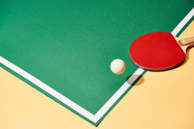 Ball and ping pong racket on yellow and green surface clipart