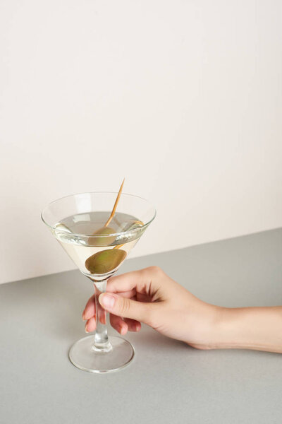 Cropped view of woman holding martini cocktail on grey surface on white background