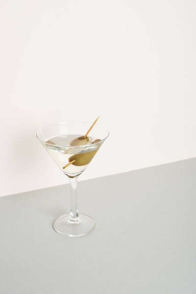 Glass of vermouth with olives on grey surface isolated on white background