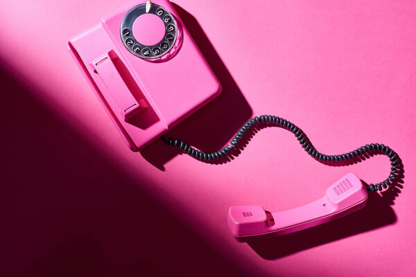 Top view of pink telephone with shadow on bright surface
