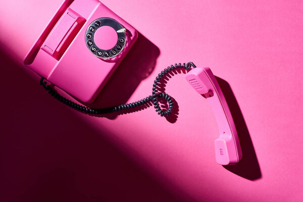 Top view of vintage pink telephone with shadow on bright surface