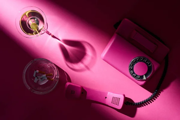 马提尼 复古电话和迷了路与烟头粉红表面的顶部视图 — 图库照片
