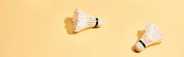 Two badminton shuttlecocks with shadow on yellow surface, panoramic shot