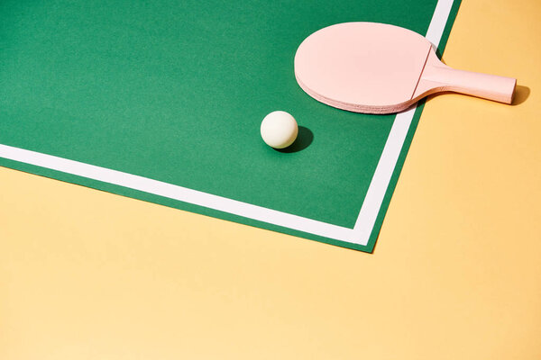 Racket and ball for ping pong on playing table on yellow background