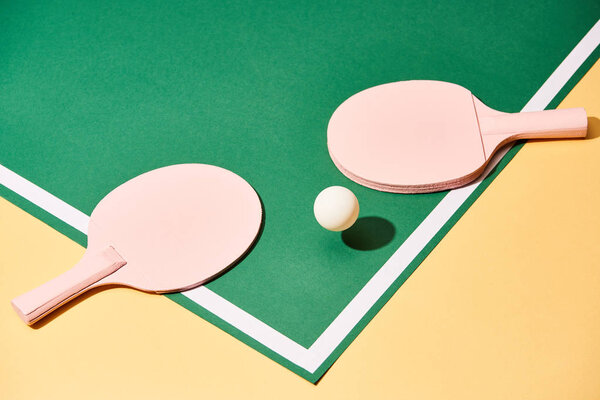Wooden rackets and ball for table tennis on green and yellow surface 