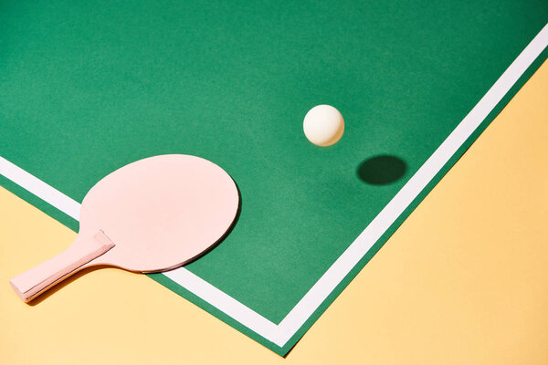 Table tennis racket and ball on green and yellow surface 