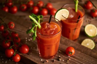 selective focus of bloody mary cocktail in glasses on wooden background with salt, pepper, tomatoes and celery clipart