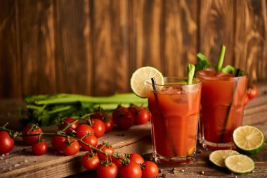  selective focus of bloody mary cocktail in glasses on wooden background with salt, pepper, lime, tomatoes and celery clipart