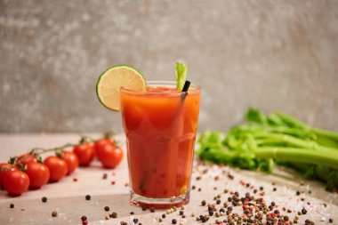 selective focus of bloody mary cocktail in glass with straw and lime near salt, pepper, tomatoes and celery on grey background clipart