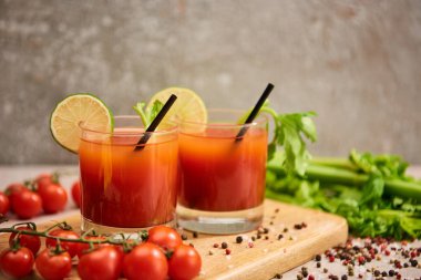Kanlı Mary kokteyli bardakta pipetle ve tahtada limonla tuz, biber, domates ve kereviz yanında.
