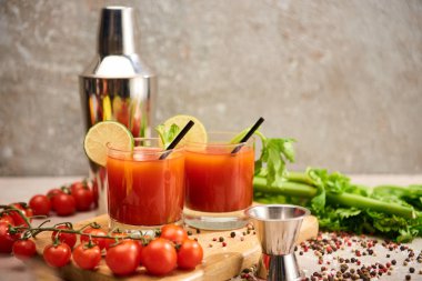 bloody mary cocktail in glasses with straws and lime on wooden board near salt, pepper, tomatoes and celery clipart