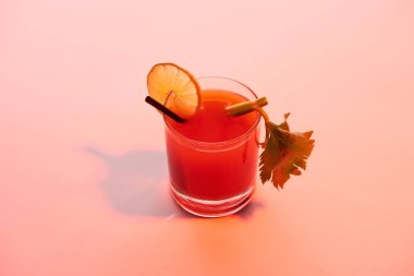 Kırmızı ışıklandırılmış arka planda limon ve kereviz ile süslenmiş kanlı Mary kokteyli.