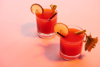 Kırmızı ışıklı arka planda limon ve kereviz ile süslenmiş gözlüklü Bloody Mary kokteyli.