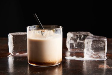 Siyah üzerine izole edilmiş eriyen buz küplerinin yanındaki camda beyaz Rus kokteyli.