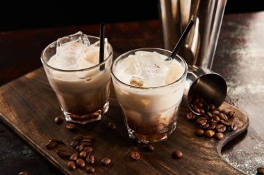 white russian cocktail in glasses with straws on wooden board with coffee grains clipart