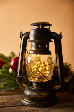 Dekoratif gaz lambası, ladin dalları ve bej üzerinde ahşap masa üzerinde noel topları.