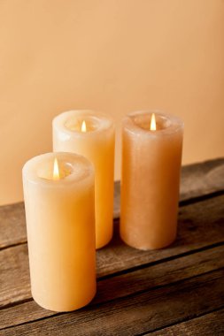 three burning candles on wooden table on beige  clipart