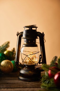 vintage oil lamp with lights, spruce branches and christmas balls on wooden table on beige clipart