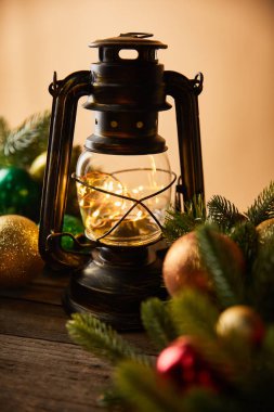 Işıkları, ladin dalları ve bej rengi Noel topları olan dekoratif klasik bir gaz lambası.