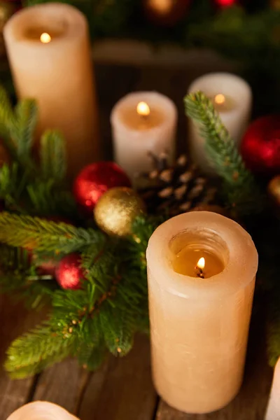 Nahaufnahme Brennender Kerzen Mit Fichtenzweigen Und Weihnachtskugeln Auf Holztisch Stockfoto