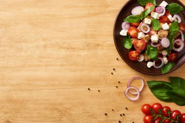 Lezzetli İtalyan sebze salatası panzanella tabakta taze malzemelerin yanında, ahşap masada servis ediliyor.