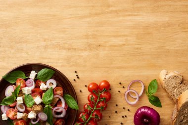 Lezzetli İtalyan sebze salatası panzanella tabakta taze malzemelerin yanında, ahşap masada servis ediliyor.