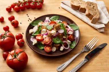 delicious Italian vegetable salad panzanella served on plate on wooden table near fresh tomatoes, bread, fork and knife clipart