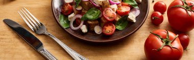 Lezzetli İtalyan sebze salatası panzanella taze domates, çatal, bıçak ve panoramik çekimin yanında ahşap masada servis edilir.
