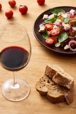 Lezzetli İtalyan sebze salatasının seçici odak noktası kırmızı şarap ve ekmeğin yanındaki tahta masada servis edilen panzanella.