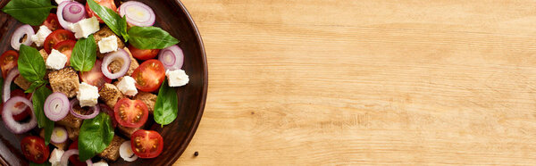 top view of fresh Italian vegetable salad panzanella served on plate on wooden table, panoramic shot