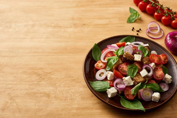美味的意大利蔬菜沙拉潘扎内拉放在靠近新鲜配料的木制桌子上的盘子里 — 图库照片