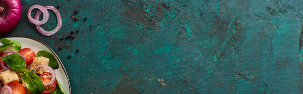 top view of delicious Italian vegetable salad panzanella served on plate on textured green surface with black pepper and red onion, panoramic shot