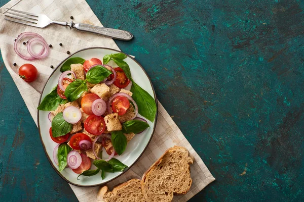 Top view of delicious Italian vegetable salad panzanella served on plate on textured green surface with bread, ingredients, napkin and fork — Stock Image Top View Delicious Italian Vegetable Salad Panzanella Served Plate Textured Royalty Free Stock Images