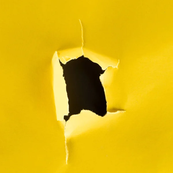 Close-up shot of hole in yellow paper isolated on black — Stock Photo